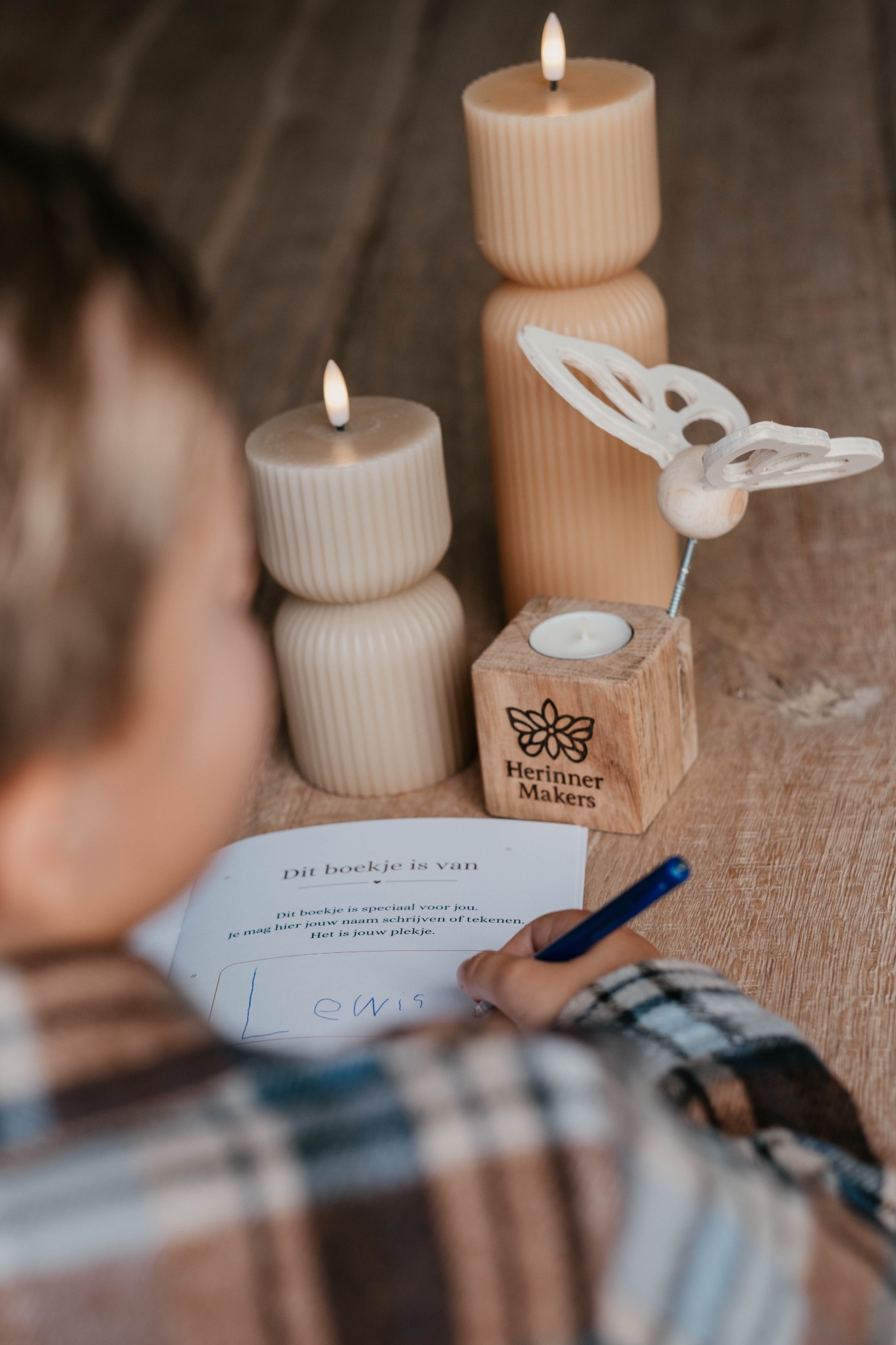 Een kind schrijft zijn naam in het herinnerboekje, met de houten vlinder op de achtergrond